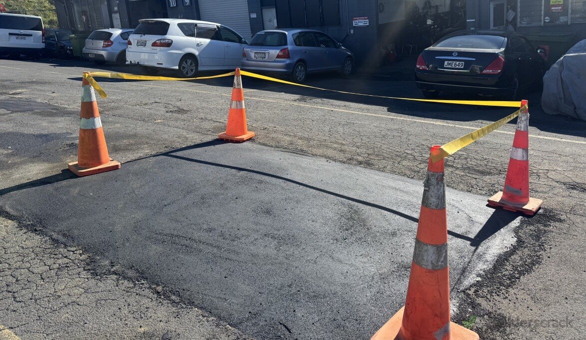 Fresh asphalt patch taped off with cones and yellow barrier tape.