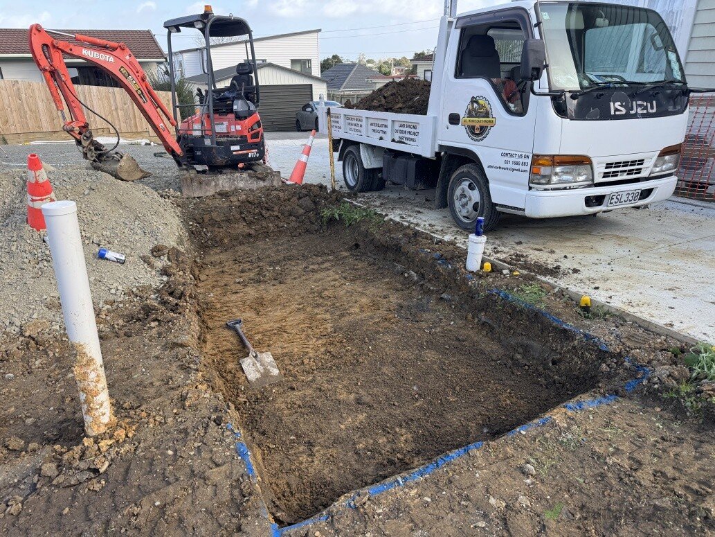 Kubota mini-excavator and branded tipper beside an open driveway excavation.